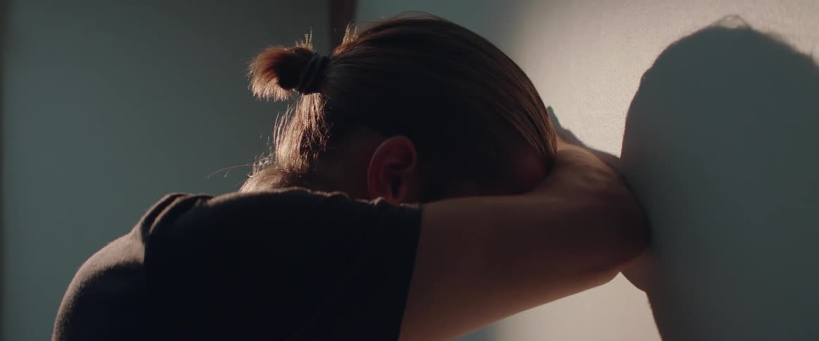 A discouraged guy with a hair bun leans against wall in deep thought.
