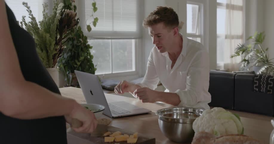 Man types on a laptop while woman cuts fruit