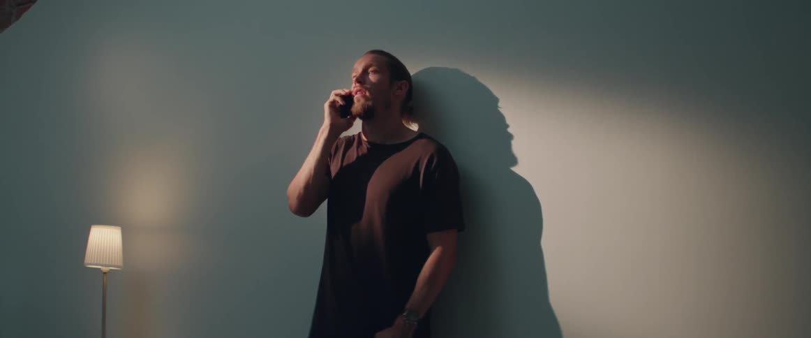 A casual person stands indoors under warm lighting while using a cell phone.