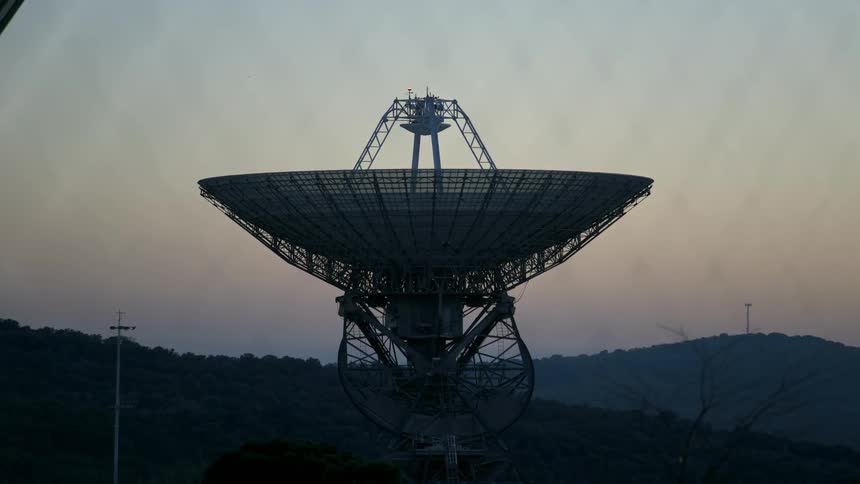 A large satellite is shown outside at dusk