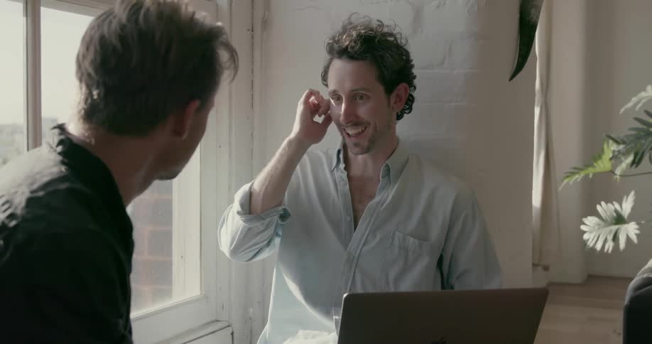 Two men talk and laugh as they sit near a window