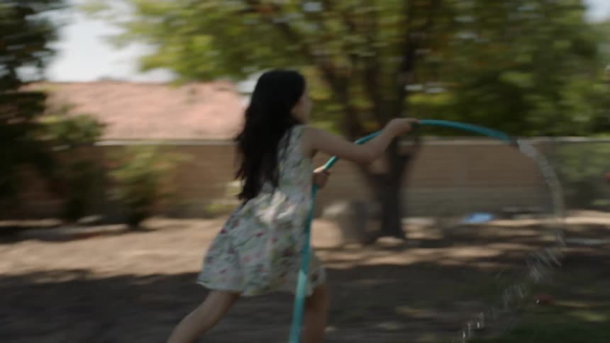 Man carries a child as a girl chases them with a water hose