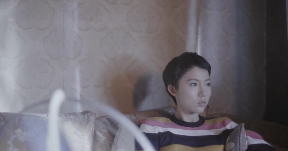 A woman sits on a couch in front of a table fan
