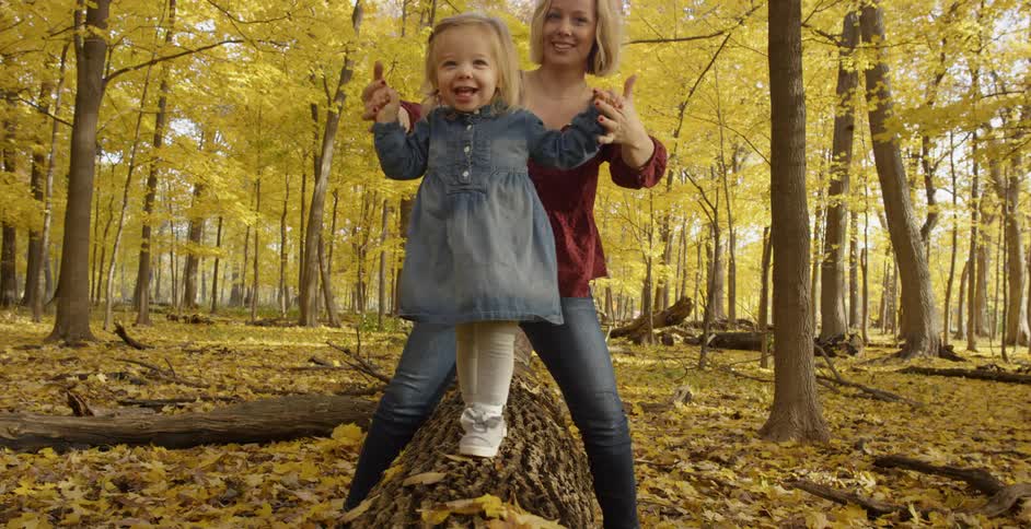 A woman walks her child over a log in the forest
