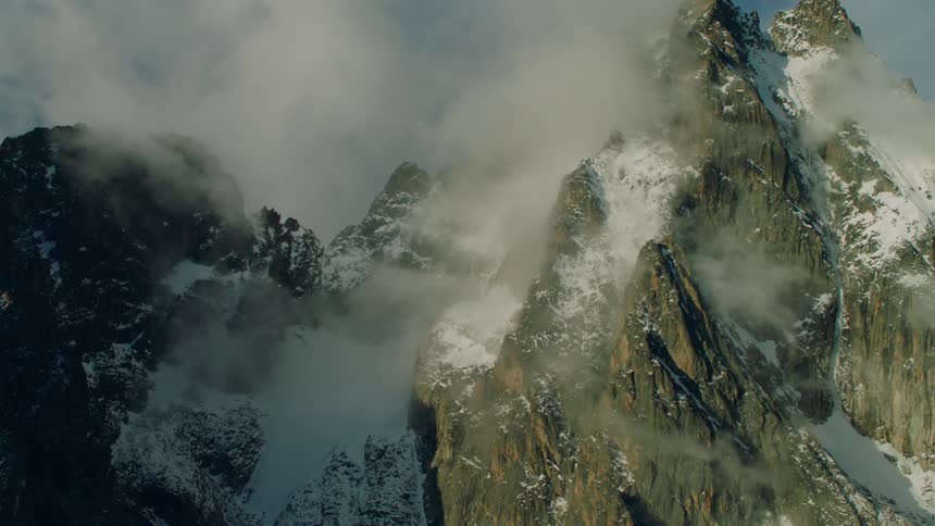 Mist surrounds the snowy mountains under a blue sky