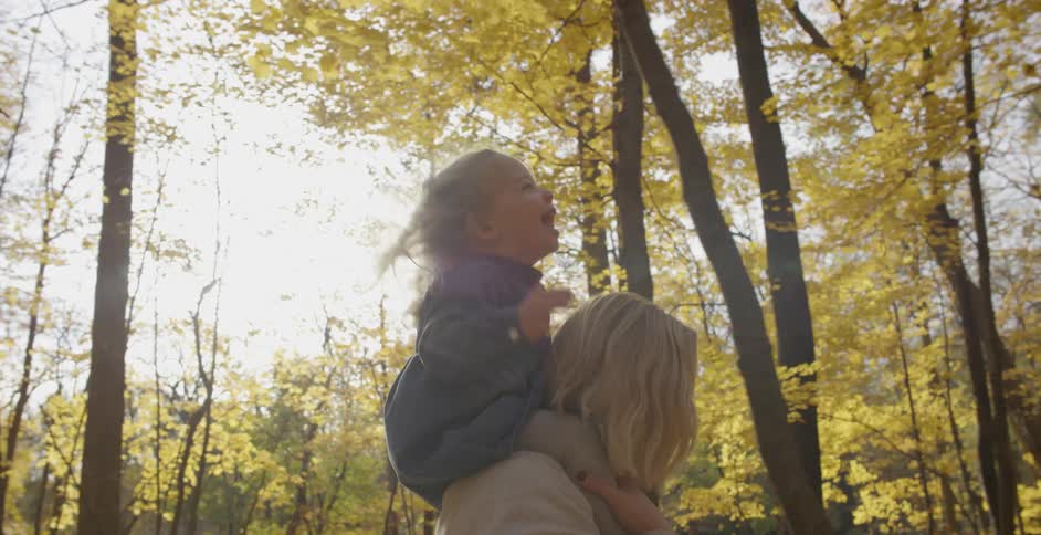 A woman is walking through the woods with a little girl on her shoulders