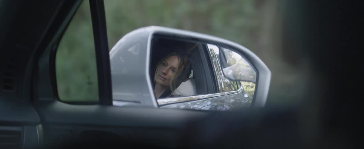 The side mirror image of a woman leaning against the window in a car