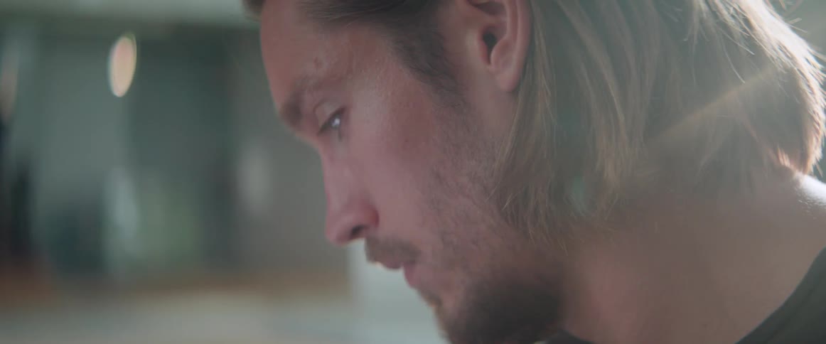 A disappointed bearded man looks down with a regretful expression inside his home.