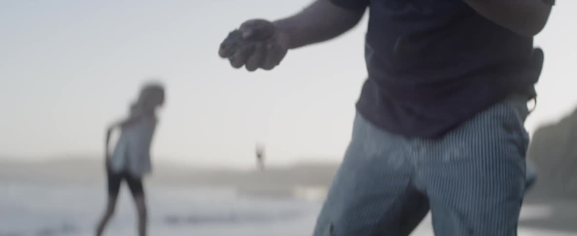 Boy throwing clumps of sand on a beach as a girl walks behind him
