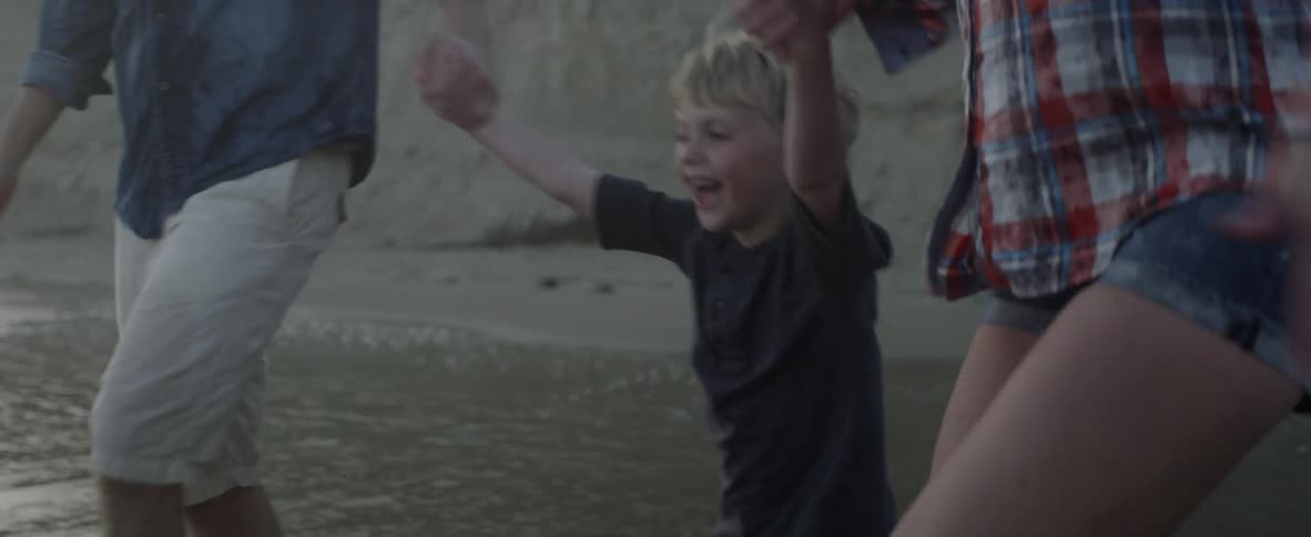 Parents swing their son between them into the surf