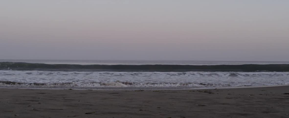Ocean waves are washing onto shore on overcast evening