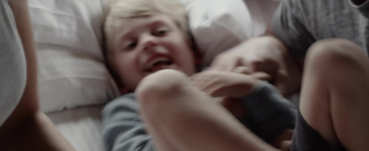 Parents are playing with their young son on a bed