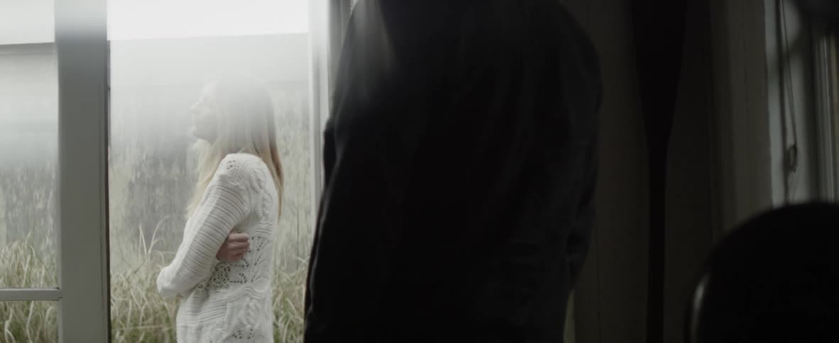 A man watches a woman standing outside in the yard