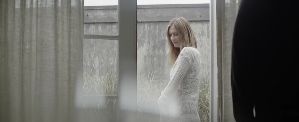 A woman stands in the garden and looks back through the open door