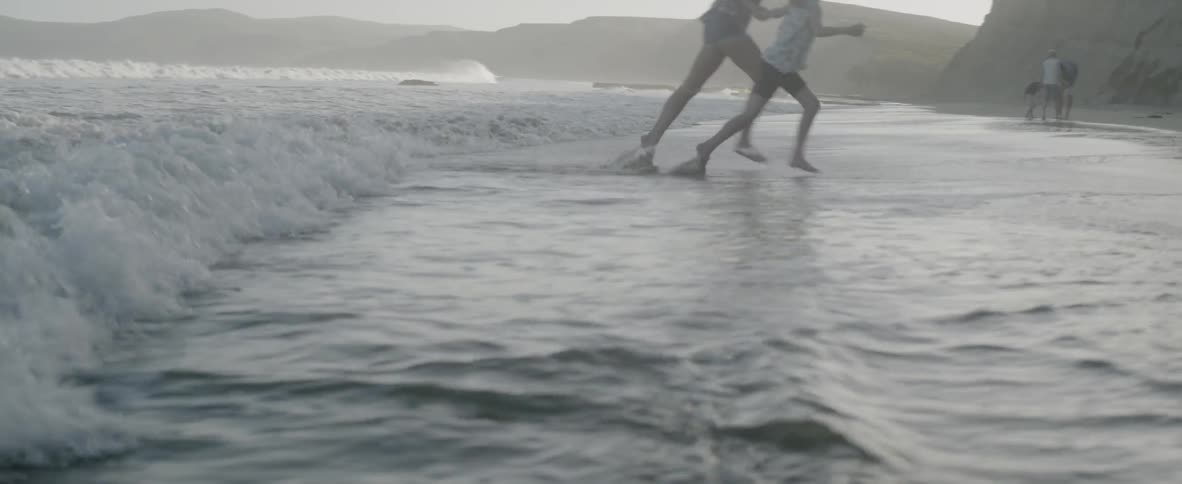 A mother and daughter run from an incoming wave, laughing their way up the sand