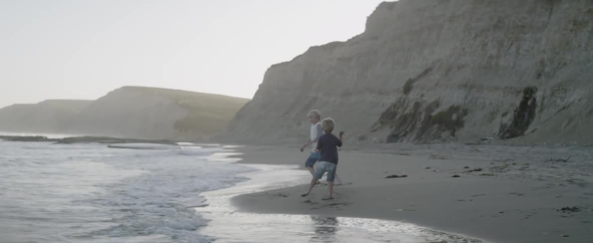 Two children throw mud at each other on the beach