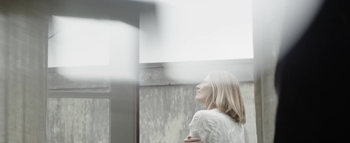 A woman is standing in the yard hugging herself and smiling in daylight