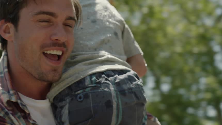 A man is holding his son as he laughs and sprays a hose