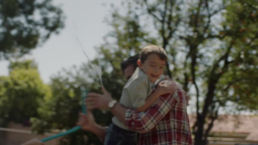 A man carries his child while spraying his hose