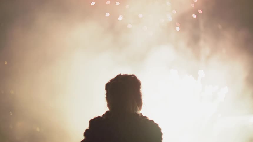 A woman watches fireworks explode in the sky