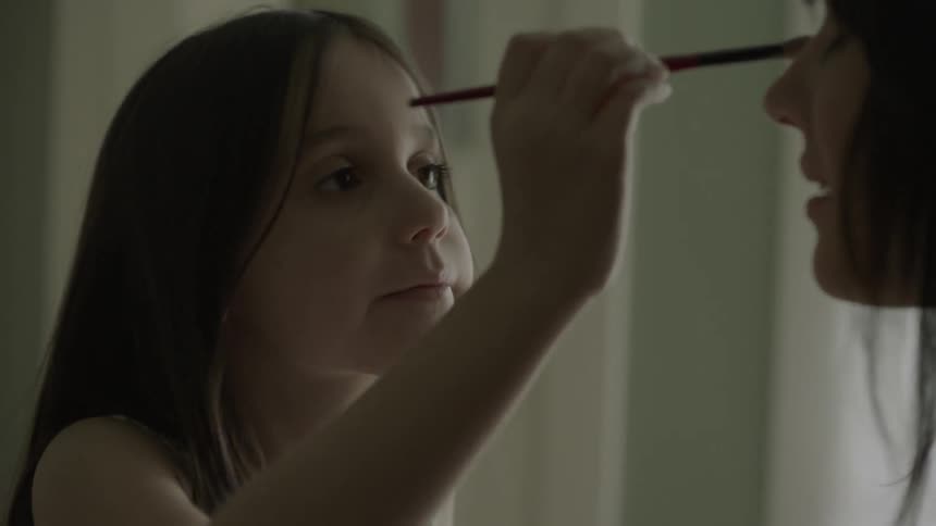 A child is putting makeup on their mother