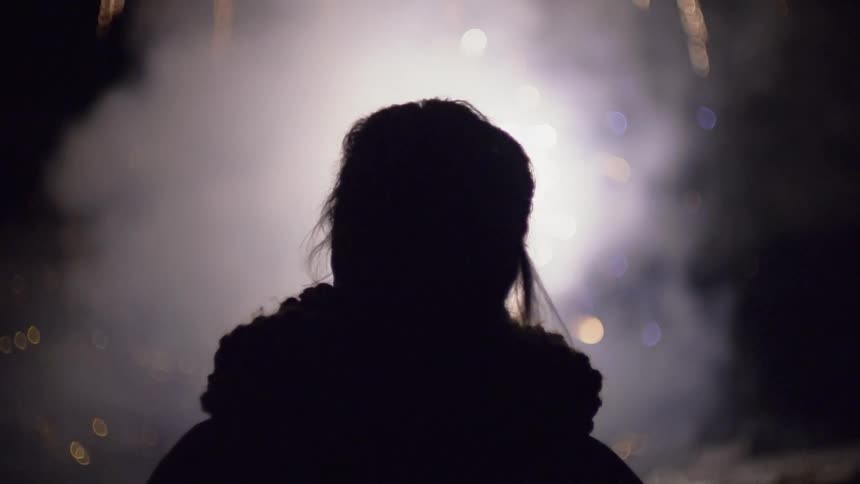 A woman is standing outside on a cold night watching fireworks