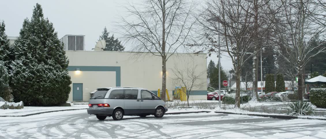 White van travels through a snowy parking lot and parks
