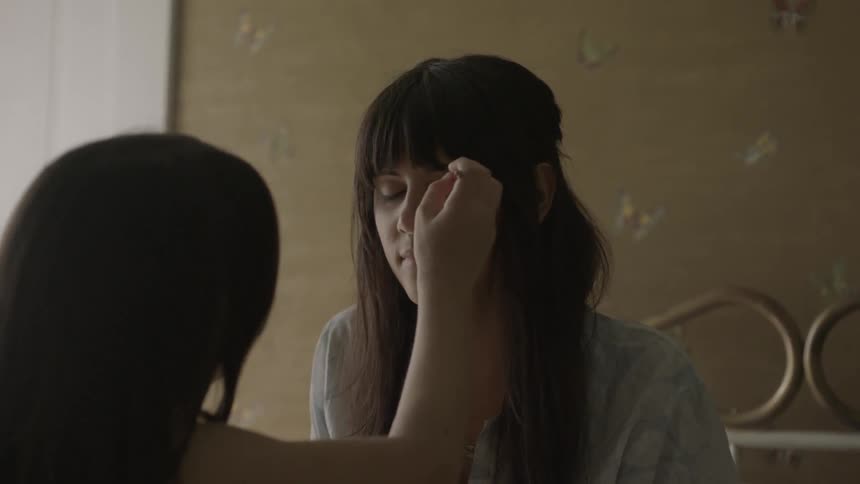 Friend applies makeup on the face of a woman in the bedroom
