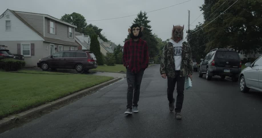 Teenagers wearing animal masks walk on a residential street