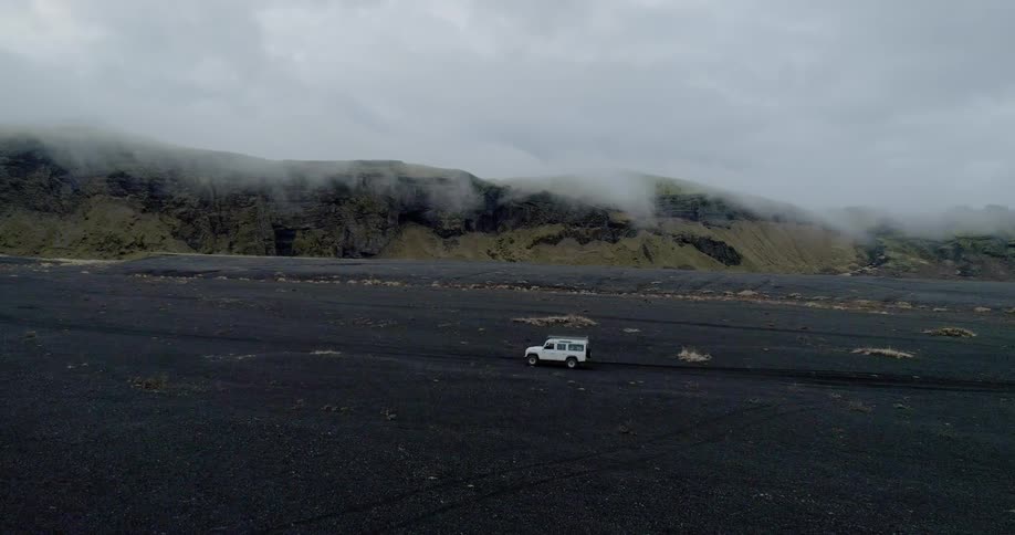 Jeep driving on black sand beach on foggy and cloudy day