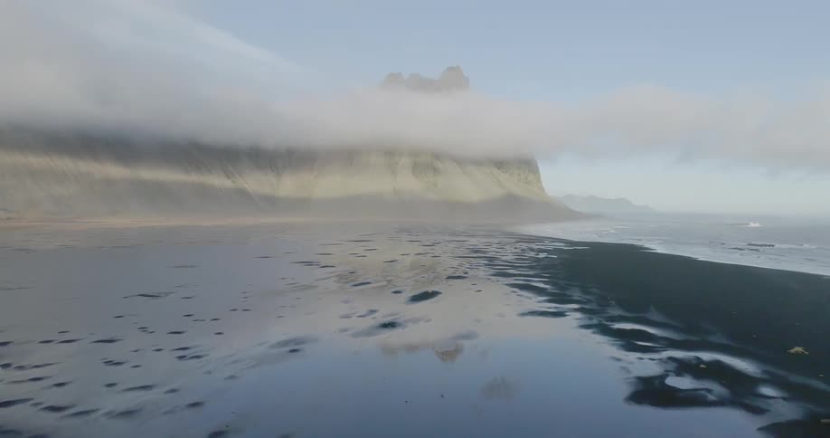 The water surrounds the mountain covered with clouds