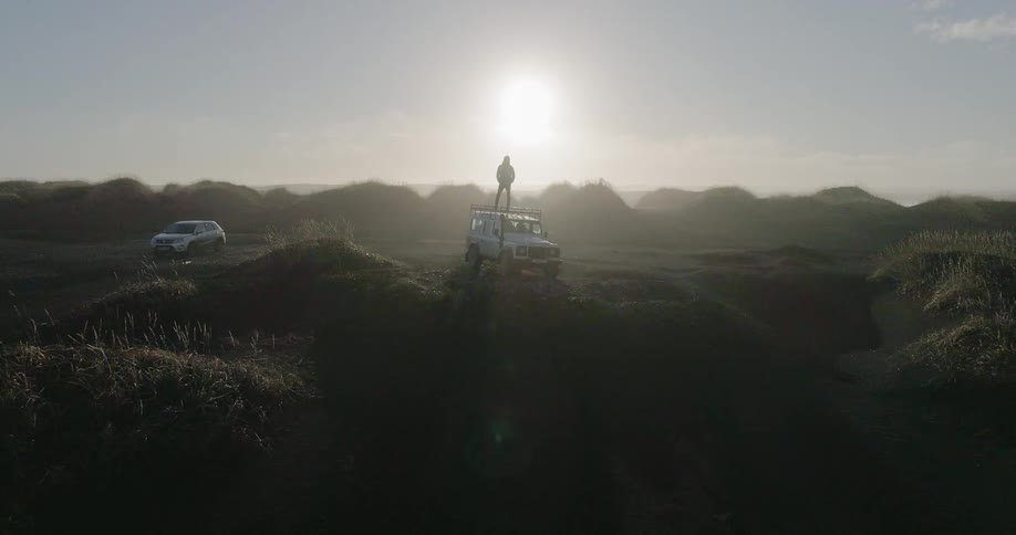 Man standing on top of jeep parked in wilderness as sun sets
