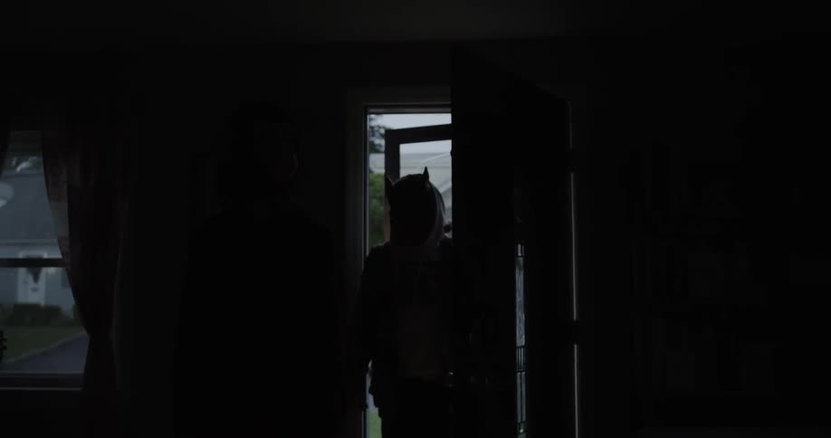 Person wearing a mask walks into a dark house