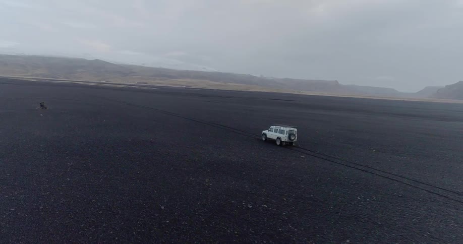 White jeep drives on flat land on a cloudy day