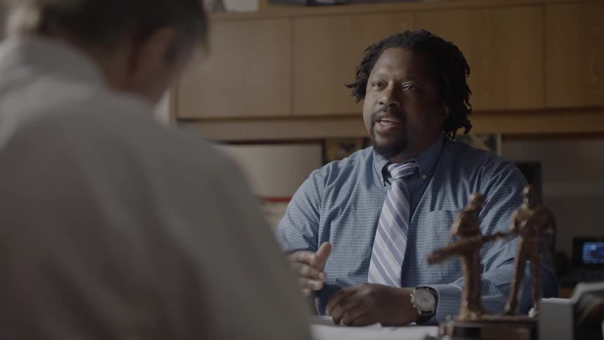 A man is talking with another at a desk