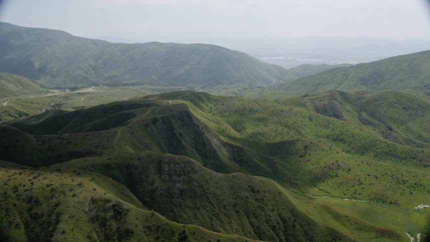 The road is full of cars traveling past the green hills