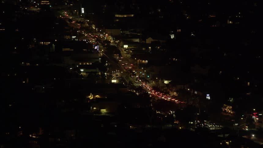 The city is dark with many cars driving down the main road at night
