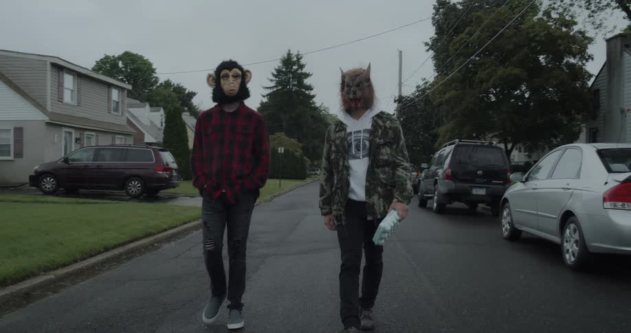 Two people in halloween masks walk down the street carrying eggs