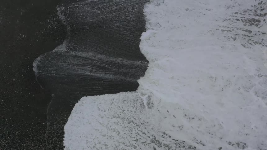 Waves come to shore on a black sand beach