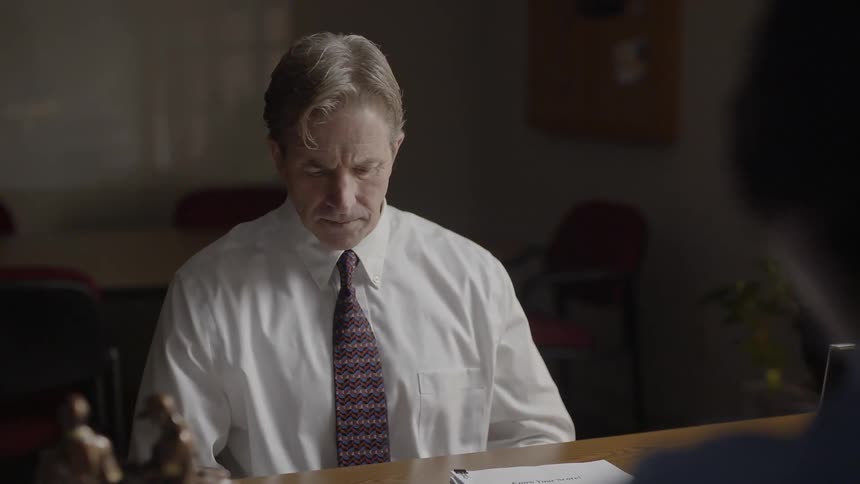 A man looks down as a person across the desk talks