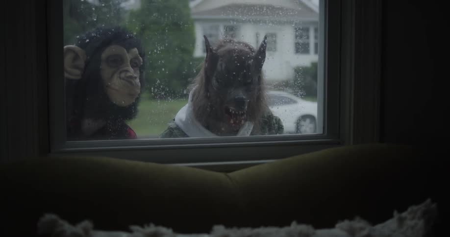 Two kids in halloween masks peek in the window on a rainy day