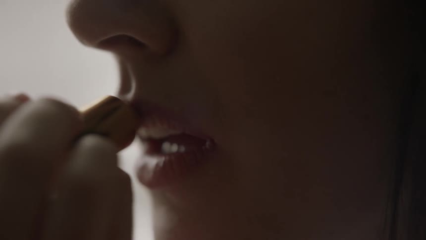 A woman is putting on lipstick