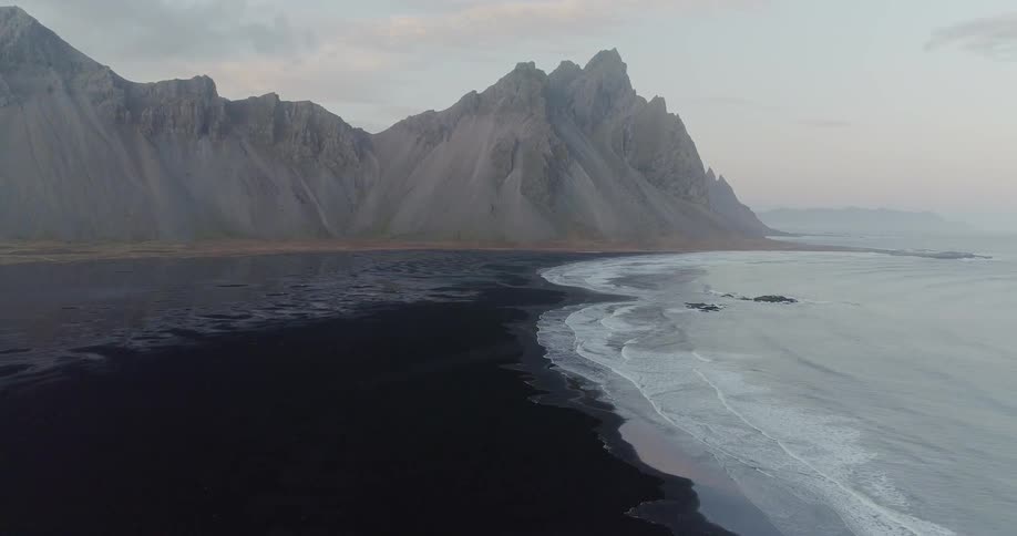 Gentle ocean waves are washing ashore on a black beach