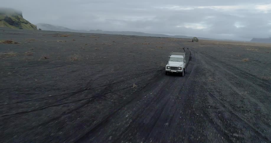 An suv leaves tracks as it travels on black sand