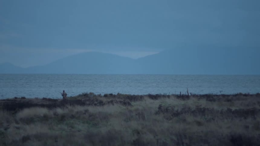 A person is firing a rifle near the shore ahead