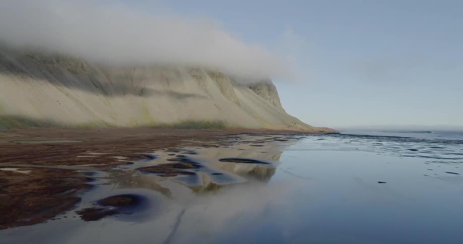 The water is calm near the cloud covered hills