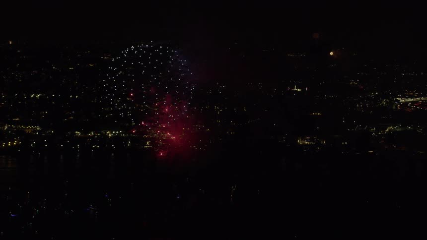 Fireworks burst in the sky above a city harbor