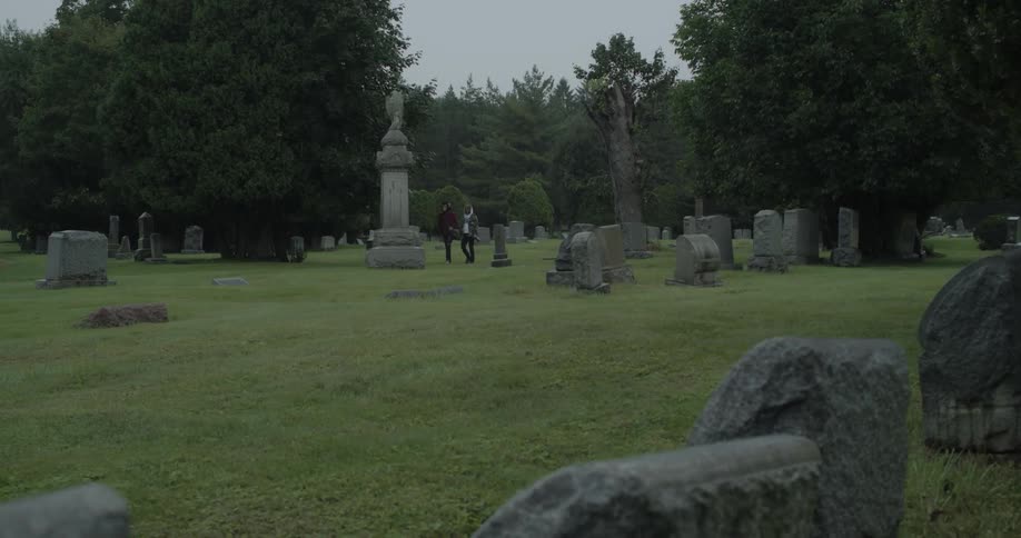 Two people slowly walk through the cemetery