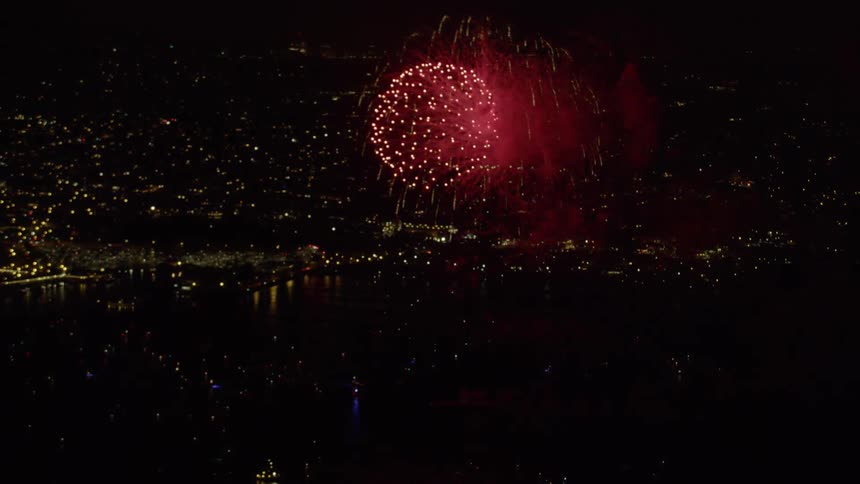 Fireworks launch from a barge and burst over the ocean