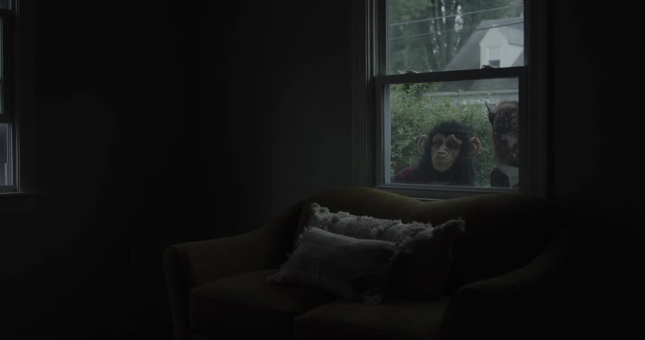 Teenagers in animal masks peek inside a house window